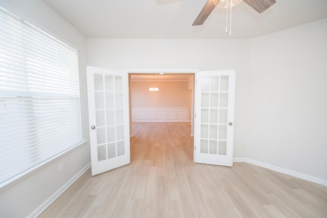 empty room with ceiling fan with notable chandelier, french doors, baseboards, and wood finished floors