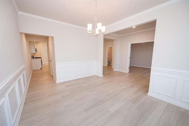 unfurnished room featuring ornamental molding, light wood-type flooring, a decorative wall, and an inviting chandelier