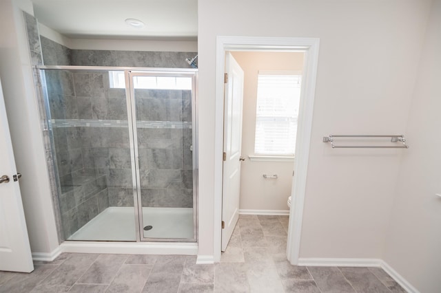 bathroom featuring a wealth of natural light, toilet, a shower stall, and baseboards