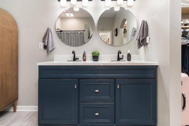 full bathroom featuring wood finished floors, a sink, baseboards, and double vanity