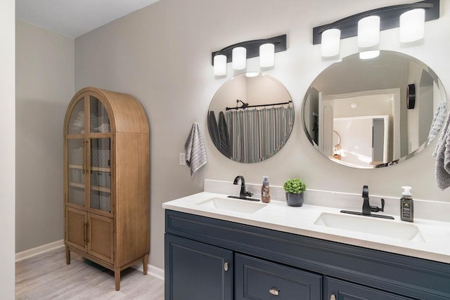 bathroom with wood finished floors, a sink, baseboards, and double vanity