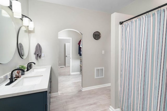 bathroom featuring double vanity, wood finished floors, a sink, and visible vents