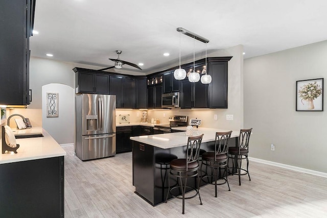 kitchen with appliances with stainless steel finishes, a kitchen breakfast bar, a peninsula, dark cabinetry, and a sink