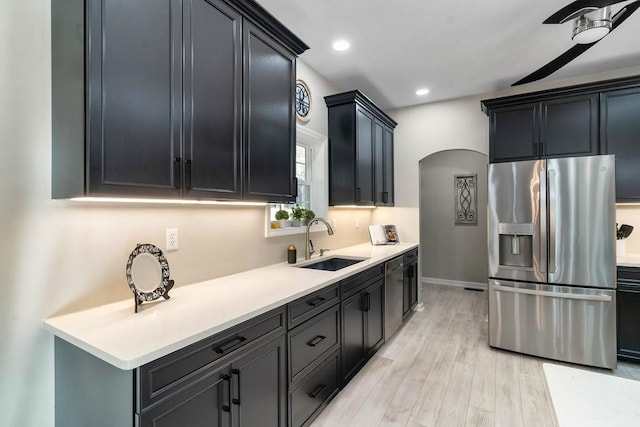 kitchen with arched walkways, light countertops, light wood-style flooring, a sink, and stainless steel fridge with ice dispenser