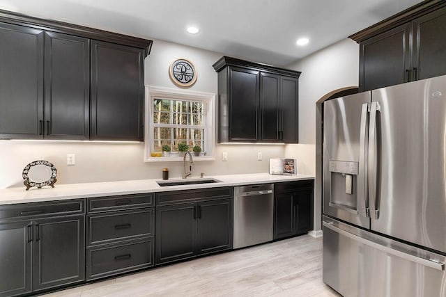 kitchen with appliances with stainless steel finishes, light countertops, dark cabinetry, a sink, and recessed lighting