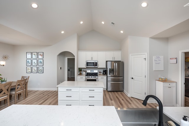 kitchen with arched walkways, light wood finished floors, stainless steel appliances, light countertops, and white cabinetry