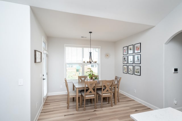 dining area featuring arched walkways, a chandelier, light wood-style flooring, visible vents, and baseboards