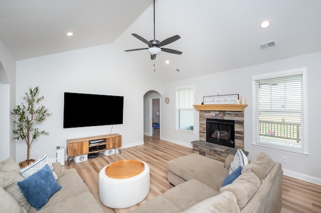 living room with arched walkways, a stone fireplace, wood finished floors, visible vents, and vaulted ceiling