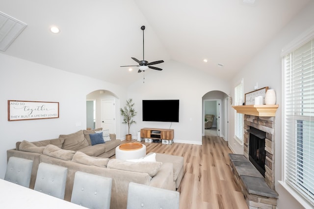 living room with arched walkways, a stone fireplace, vaulted ceiling, and light wood-style flooring