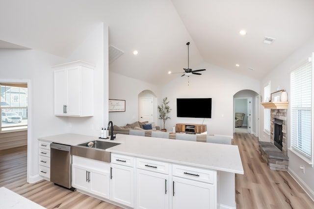 kitchen featuring visible vents, dishwasher, a peninsula, a stone fireplace, and white cabinetry