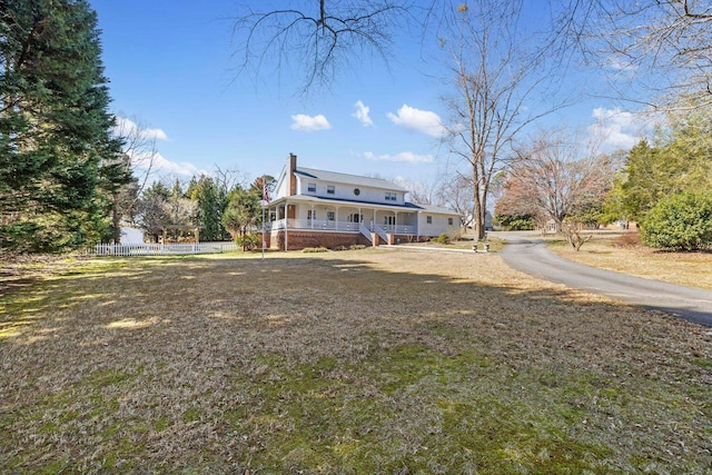 rear view of house with driveway, a chimney, fence, a yard, and a porch