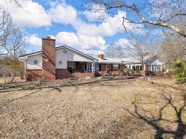 rear view of house with covered porch, brick siding, and a chimney