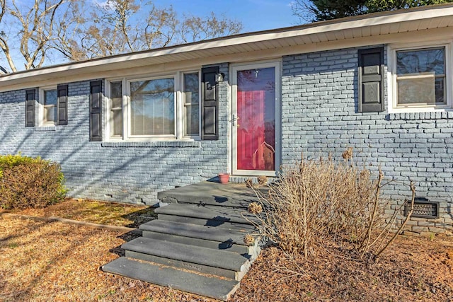 view of exterior entry with crawl space and brick siding