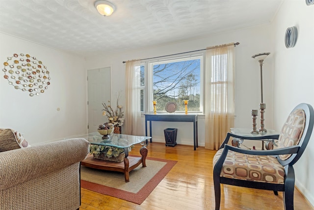 sitting room featuring a textured ceiling, ornamental molding, light wood-style flooring, and baseboards