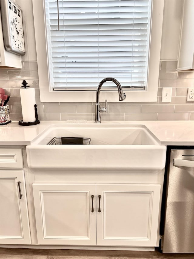 kitchen featuring a sink, white cabinetry, light countertops, stainless steel dishwasher, and decorative backsplash