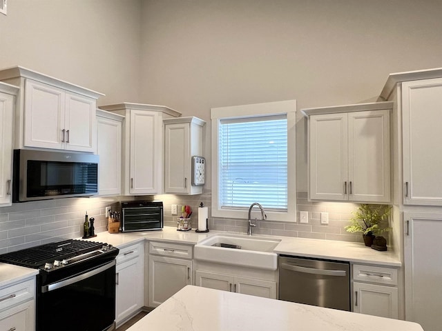 kitchen featuring appliances with stainless steel finishes, white cabinets, a sink, and decorative backsplash