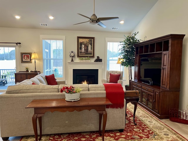 living area featuring a warm lit fireplace, visible vents, a ceiling fan, and recessed lighting