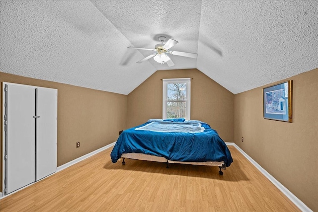 bedroom with lofted ceiling, a ceiling fan, a textured ceiling, wood finished floors, and baseboards