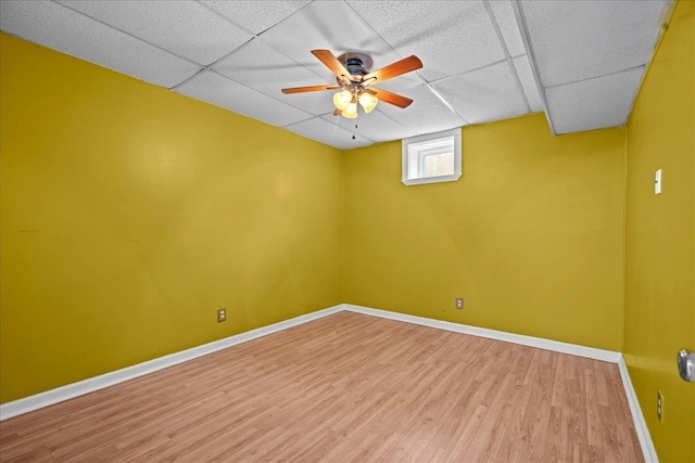 below grade area featuring a paneled ceiling, ceiling fan, baseboards, and wood finished floors