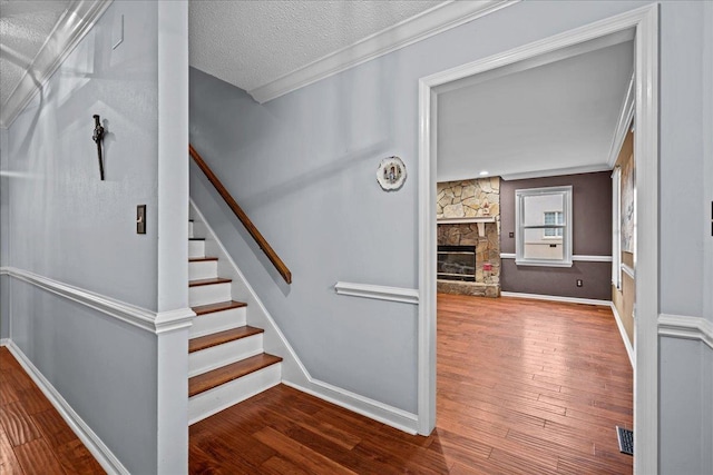 stairway featuring crown molding, a stone fireplace, a textured ceiling, and hardwood / wood-style flooring