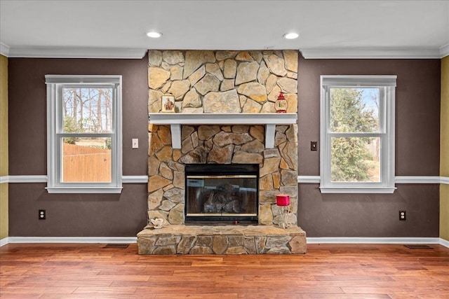 unfurnished living room featuring a wealth of natural light, crown molding, a stone fireplace, and wood finished floors