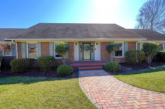 ranch-style home with brick siding, a front lawn, and a shingled roof