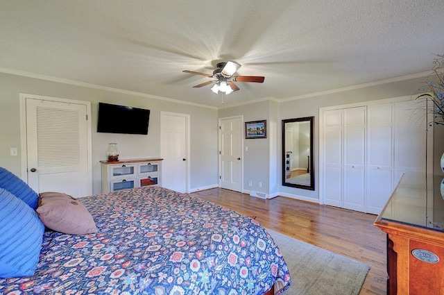 bedroom featuring multiple closets, ornamental molding, ceiling fan, a textured ceiling, and wood finished floors