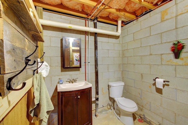 bathroom with concrete flooring, vanity, toilet, and concrete block wall