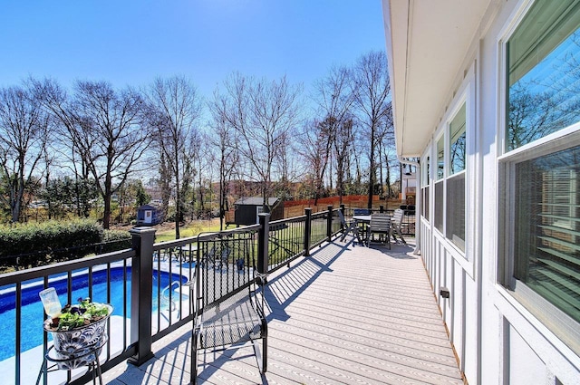 wooden deck with an outbuilding, a storage shed, outdoor dining area, and a fenced in pool