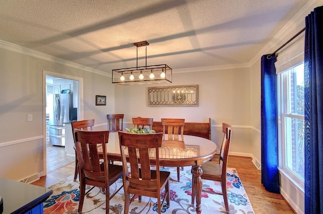 dining area featuring ornamental molding, light wood-type flooring, a textured ceiling, and baseboards