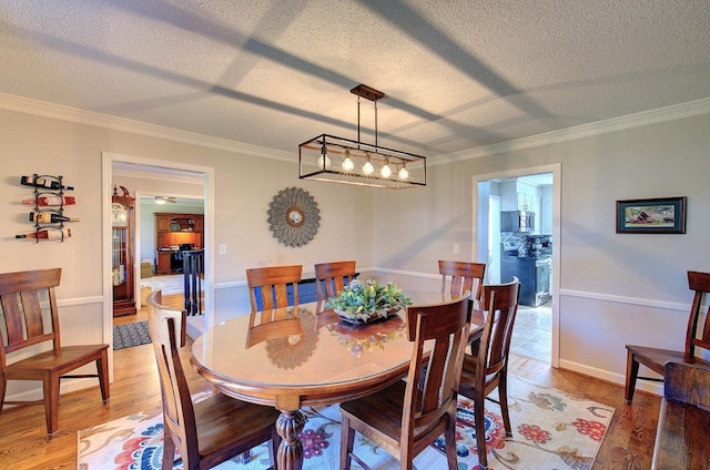 dining room with light wood-style floors, crown molding, a textured ceiling, and baseboards