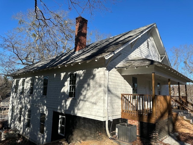 view of side of property featuring a porch, a chimney, and central AC unit