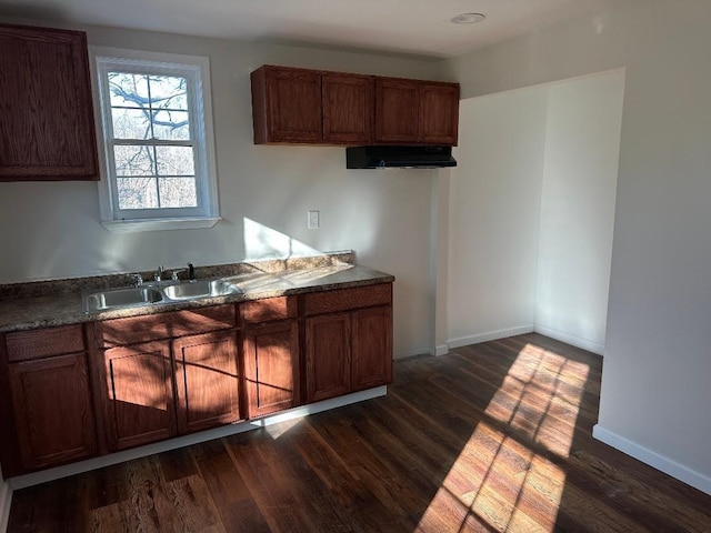 kitchen with dark wood-style floors, dark countertops, a sink, and baseboards