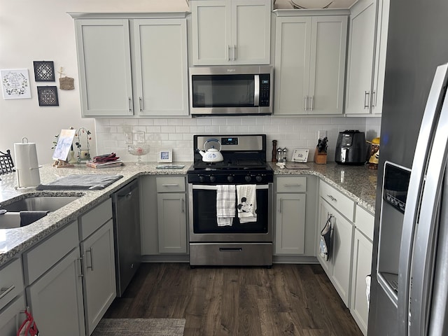 kitchen featuring light stone counters, dark wood-type flooring, a sink, appliances with stainless steel finishes, and backsplash