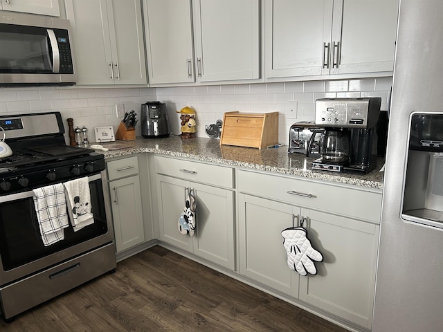 kitchen featuring stainless steel appliances, dark wood-type flooring, light stone counters, and decorative backsplash