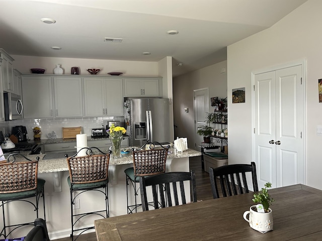 kitchen featuring stainless steel appliances, a peninsula, visible vents, a kitchen breakfast bar, and tasteful backsplash