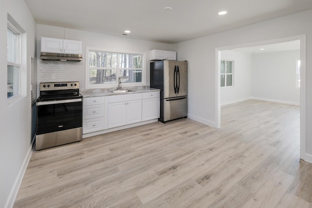 kitchen with light wood finished floors, stainless steel appliances, white cabinets, a sink, and under cabinet range hood