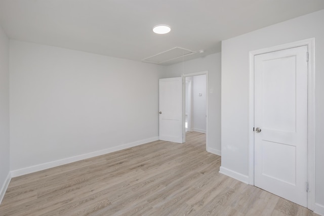 unfurnished bedroom with light wood-style floors, attic access, and baseboards