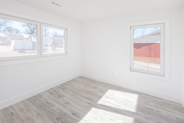 empty room with a wealth of natural light, wood finished floors, visible vents, and baseboards