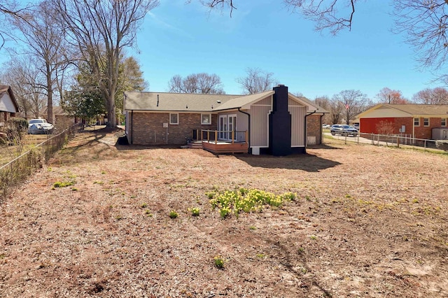 rear view of house featuring brick siding, a wooden deck, and fence