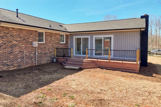 back of house with a shingled roof, a chimney, brick siding, and a deck