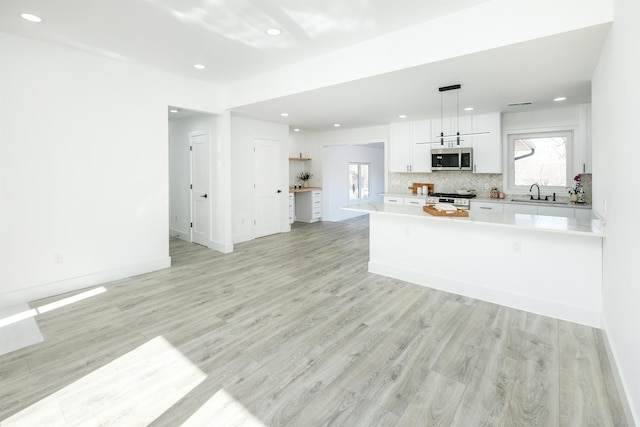 kitchen featuring light wood finished floors, stainless steel appliances, tasteful backsplash, light countertops, and white cabinetry