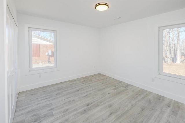 unfurnished room with light wood-style floors, a wealth of natural light, and baseboards