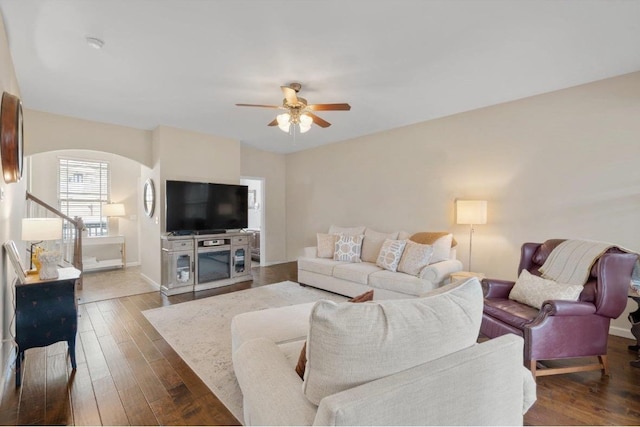 living room with arched walkways, dark wood finished floors, a ceiling fan, and baseboards