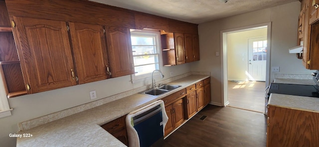 kitchen with brown cabinets, light countertops, dark wood-type flooring, a sink, and dishwashing machine