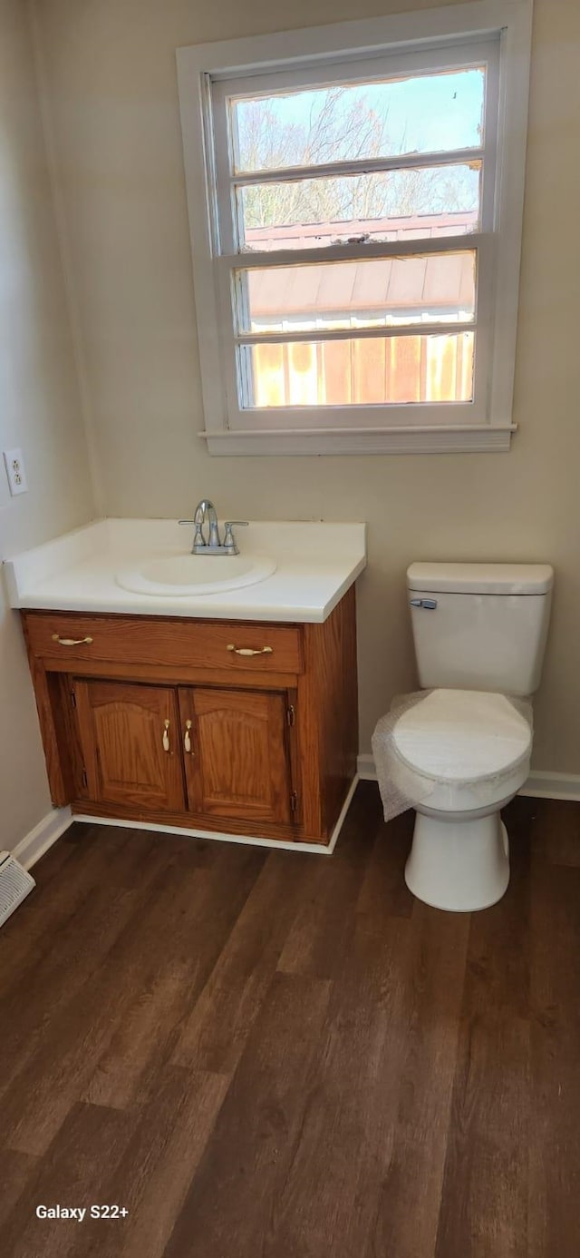 half bathroom with toilet, baseboards, wood finished floors, and vanity