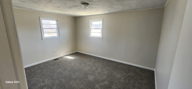 spare room with crown molding, baseboards, dark colored carpet, and a wealth of natural light