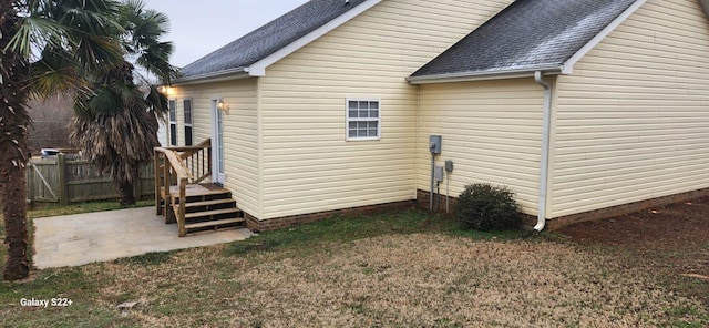 view of side of property featuring a patio, roof with shingles, and fence