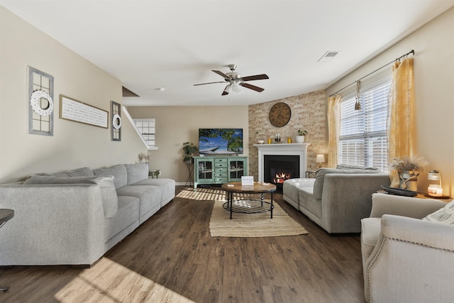 living room featuring dark wood finished floors, visible vents, ceiling fan, a warm lit fireplace, and baseboards