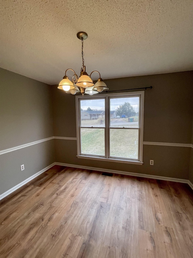 unfurnished dining area with a textured ceiling, wood finished floors, visible vents, and baseboards